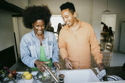 Happy friends doing housework together in kitchen at home