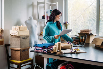 Young woman tailor fashion designer dressmaker using laptop in seamstress studio