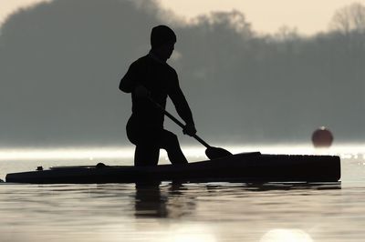 Silhouette man standing by lake against sky