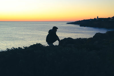 Silhouette people sitting on beach during sunset