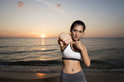 Portrait of smiling young woman standing at beach against sky