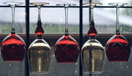 Close-up of upside down wineglasses hanging against window