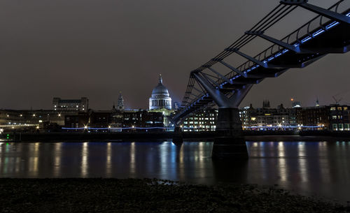 Illuminated bridge over river by buildings against sky at night