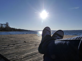 Low section of man relaxing on pier at sea against sky