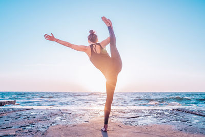 Full length of woman doing yoga at beach against sky during sunset