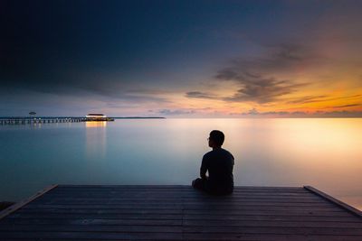 Rear view of man sitting on sea against sky