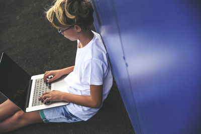 High angle view of boy using laptop while sitting by wall indoors