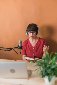 Senior woman reading book sitting against wall