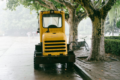 Yellow vehicle on wet road by trees in city