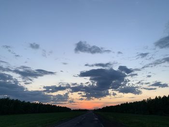 Road amidst field against sky during sunset