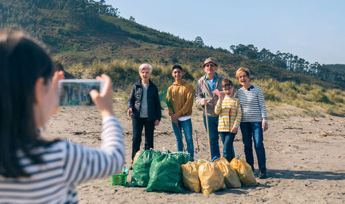 Girl photographing family picking garbage at beach