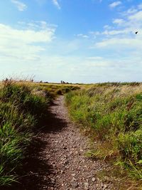 Dirt road in field against cloudy sky