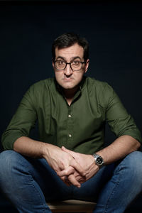 Portrait of man sitting against black background