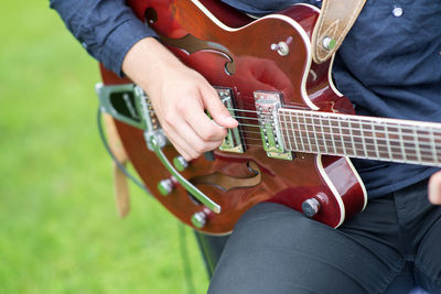 Midsection of man playing guitar while sitting in park