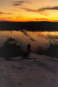 Silhouette man by lake against sky during sunset