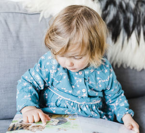 Cute girl reading book while sitting at home