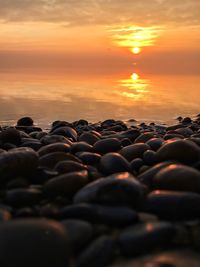 Stones in sea against sky during sunset