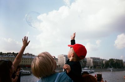 Rear view of people with bubbles against sky