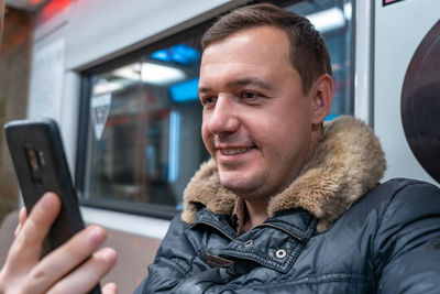 Smiling man using mobile phone at subway train