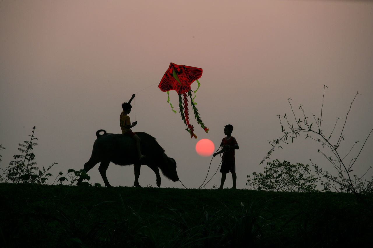 PEOPLE STANDING ON FIELD AGAINST CLEAR SKY DURING SUNSET