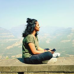 Side view of young woman using smart phone against mountains