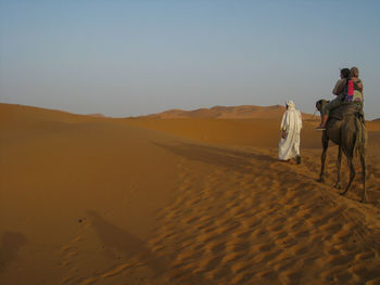 Rear view of woman riding motorcycle on desert against clear sky