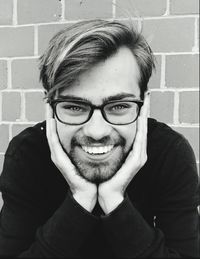 Close-up portrait of smiling young man sitting against brick wall