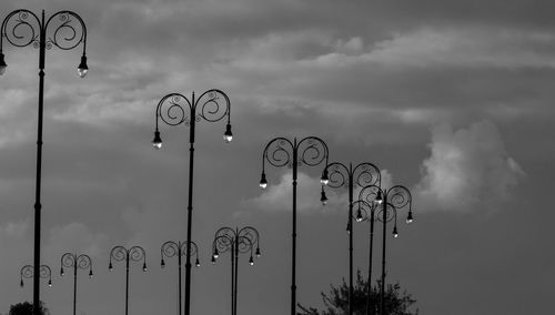 Low angle view of street lights in row against cloudy sky during dusk