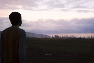 Rear view of man standing on field against cloudy sky during sunrise