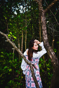 Young woman standing by tree trunk in forest