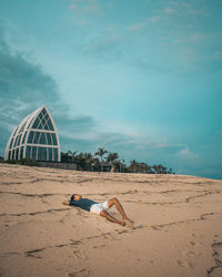 Man relaxing on sand at beach against sky