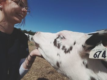 Smiling woman petting cow on field against sky during sunny day