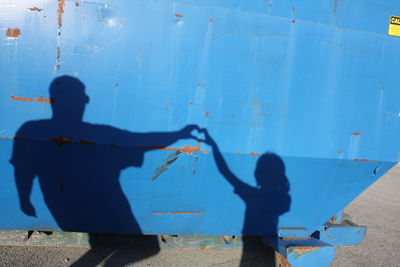 Shadow of man and child making heart shape on blue metallic structure during sunny day