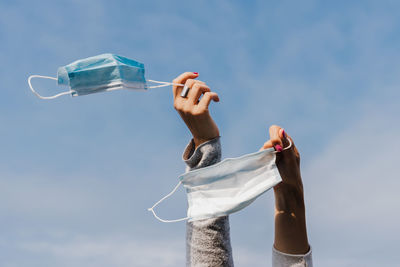 Unrecognizable two woman hands holding face mask during pandemic corona virus outdoors over blue sky