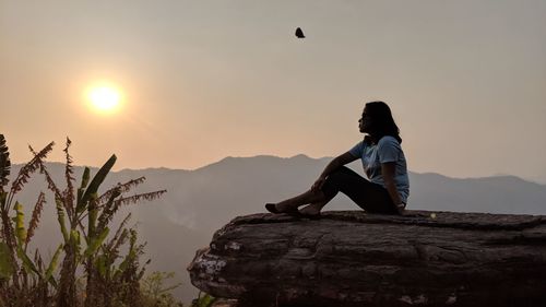 Woman sitting on mountain against sky during sunset