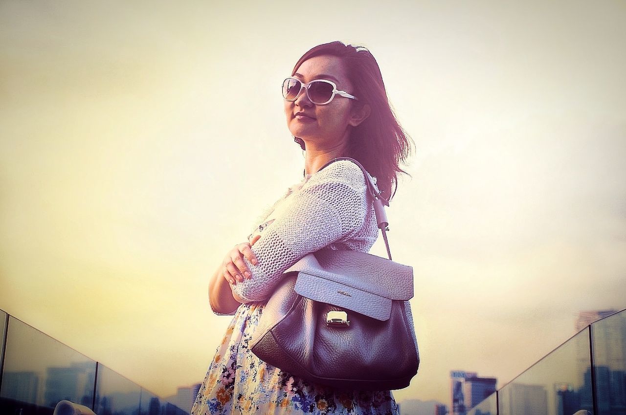 glasses, one person, real people, lifestyles, women, young adult, young women, sky, leisure activity, standing, fashion, sunglasses, casual clothing, architecture, hairstyle, beautiful woman, low angle view, beauty, outdoors