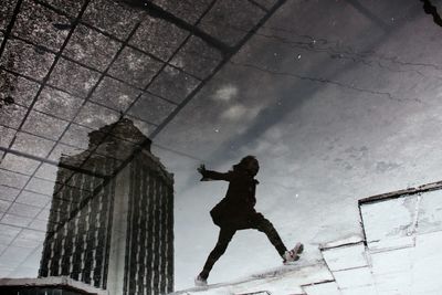 Upside down image of man jumping by puddle on footpath in city