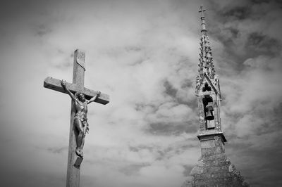 Low angle view of cross fix statue by bell tower against cloudy sky