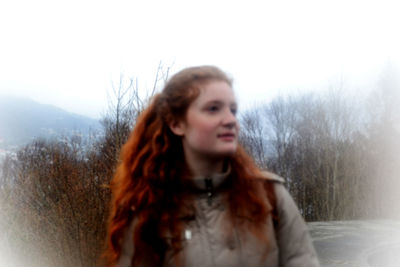 Portrait of beautiful young woman standing by snow against sky