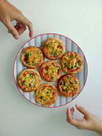 High angle view of people reaching towards plate of mini pizzas