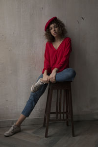 Portrait of young woman sitting on chair against wall