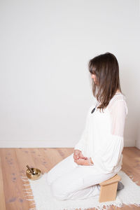 Beautiful adult woman dressed in white during a meditation sesion. wooden bench and cupper bowl.