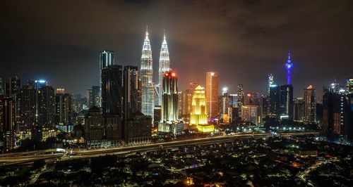 Illuminated modern buildings in city against sky at night