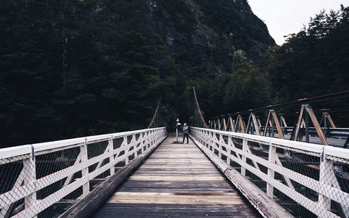 Mid distance of person standing on footbridge against mountain