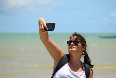 Young woman taking selfie at beach against sky