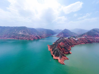 Scenic view of sea by mountain against sky