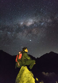 Young man sitting on a rock in the andes mountain range with the milky