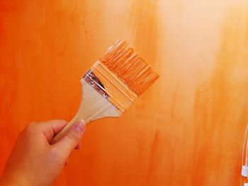 Cropped hand panting orange wall at home