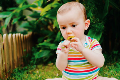 Cute baby girl biting flower at back yard