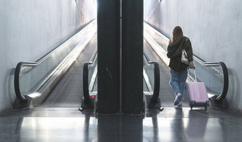 Young woman with suitcase walking towards moving walkway at railroad station